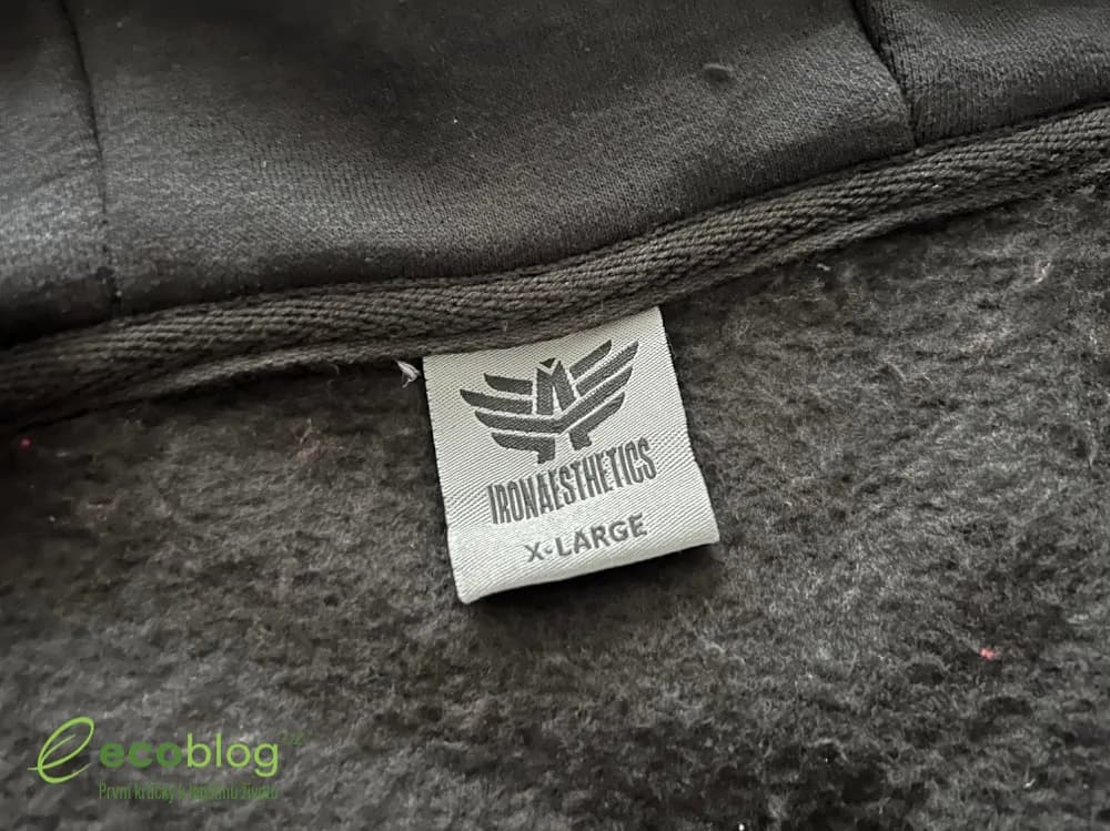 Detail šedé visačky Iron Aesthetics s logem a velikostí X-Large našité v černé mikině s počesem