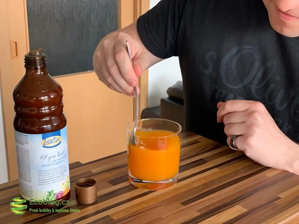Hotový oranžový nápoj LaVita ve sklenici vedle lahve koncentrátu