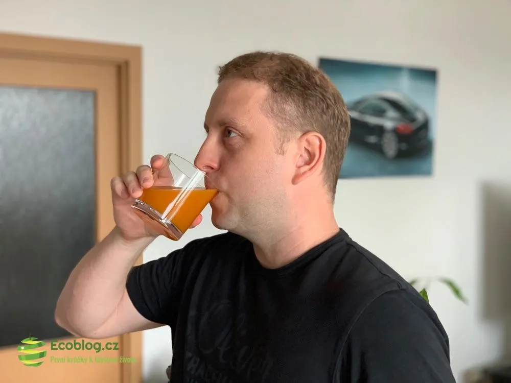 Muž pije oranžový nápoj LaVita ze sklenice v obývacím pokoji