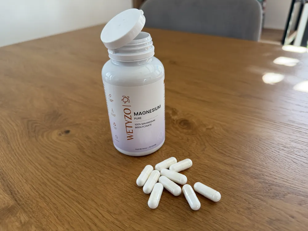 Otevřená lahvička WETYZO Magnesium Pure s bílými kapslemi na stole